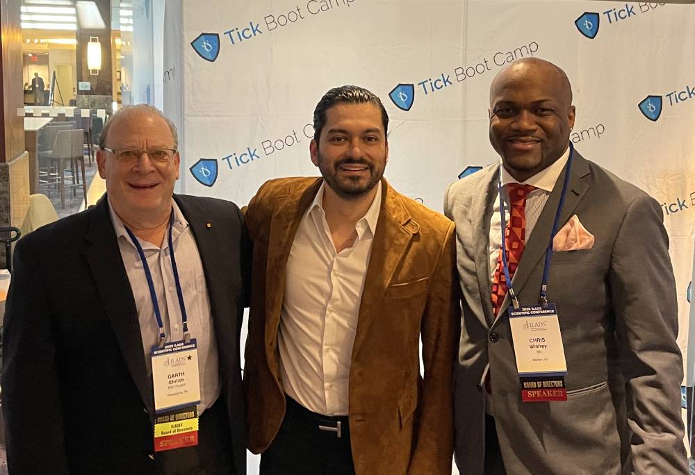 Tick Boot Camp at ILADS 2026: Official Podcast & Gala Emcees 5 Drs. Garth Ehrlich, Omar Morales, and Chris Winfrey at the Tick Boot Camp podcast backdrop.